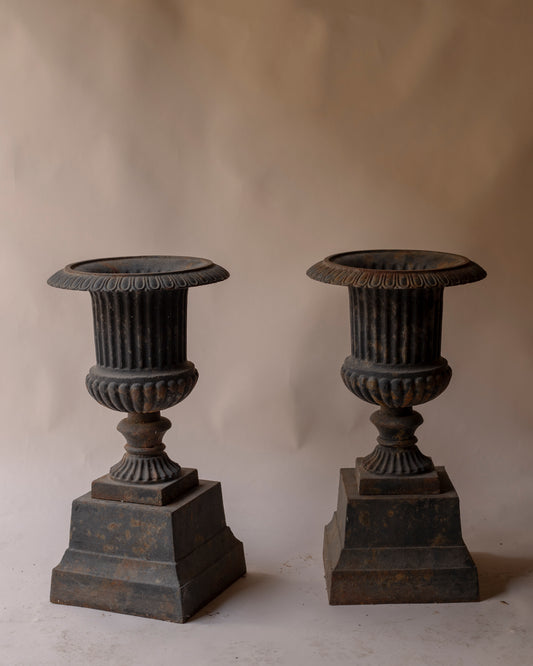 Pair of grey cast iron urns with plinth